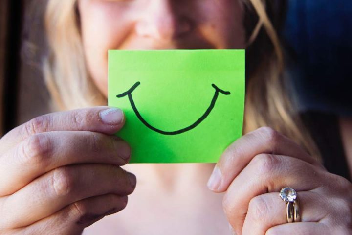 Woman holding up paper with smile drawn on it